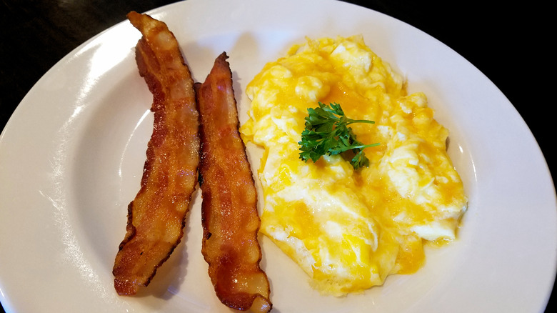 scrambled eggs with cheese and bacon on white plate