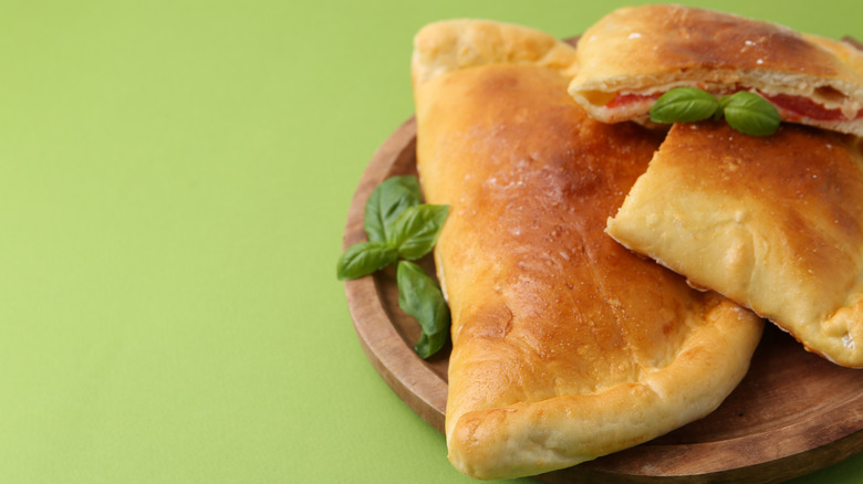 calzones with tomato, cheese, and basil on green background