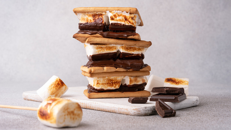 S'mores stacked on wooden board with ingredients laying on the side