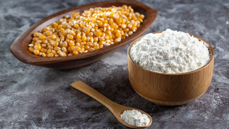 Cornstarch placed in a bowl and spoon with corn kernels in the background