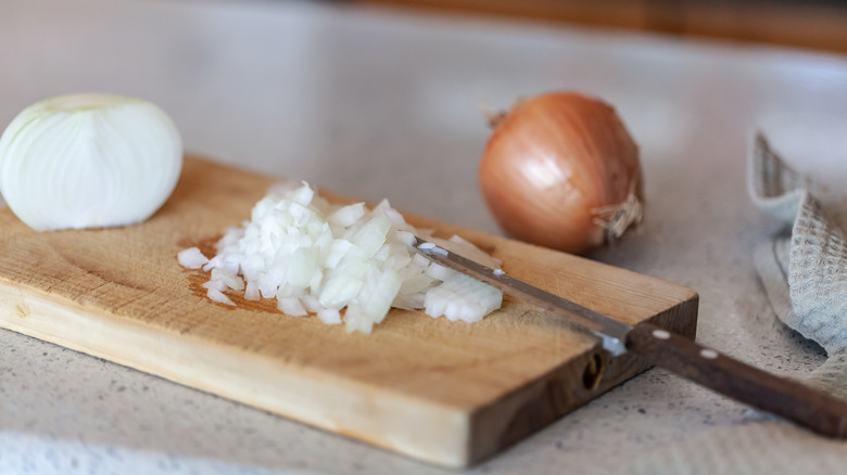Chopped onion placed on a chopping board with a knife and onion in the background