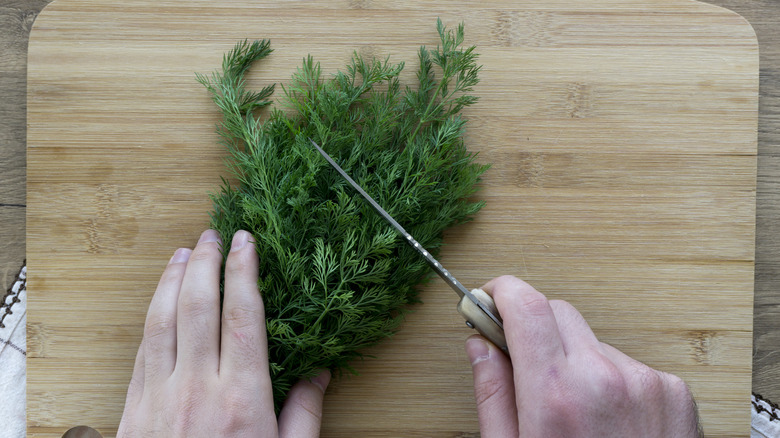 Hands chopping fresh dill on wooden cutting board