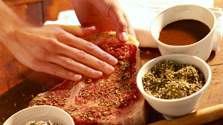 Person rubbing marinade on a big t bone steak