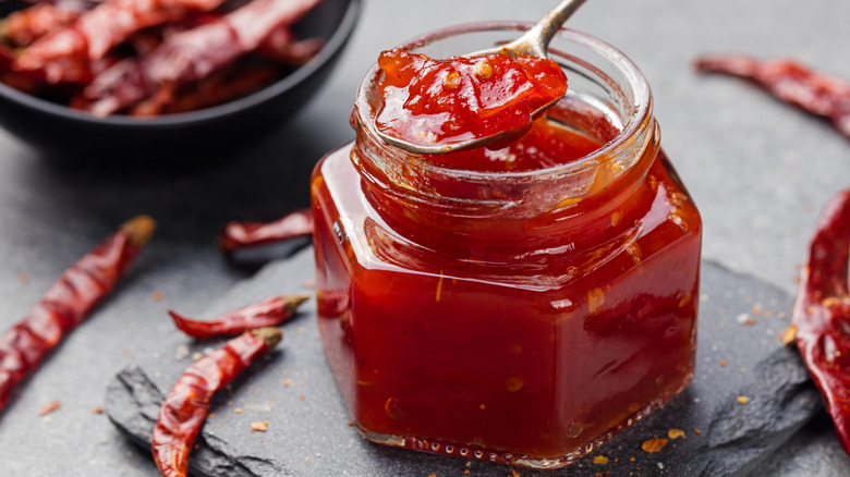 Tomato and chili sauce, jam, confiture in a glass jar on a grey stone background