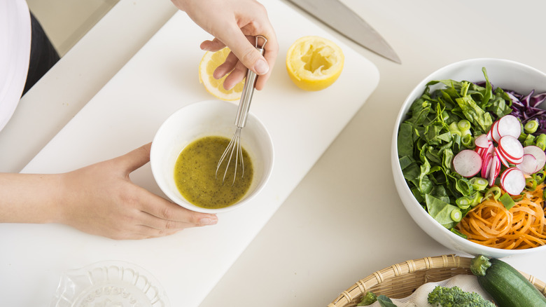 Person whisking vinaigrette in a white bowl with bowl of salad nearby