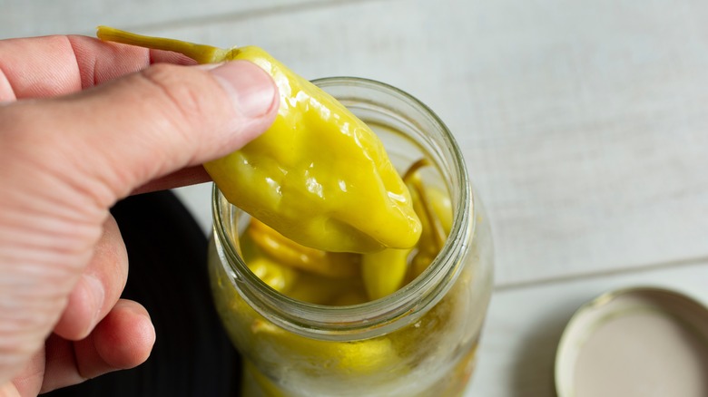 Hand taking a pepperoncini out of a jar