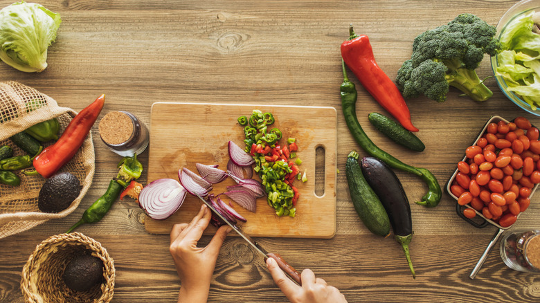 Overhead of person cutting onions and peppers on a wooden cutting board