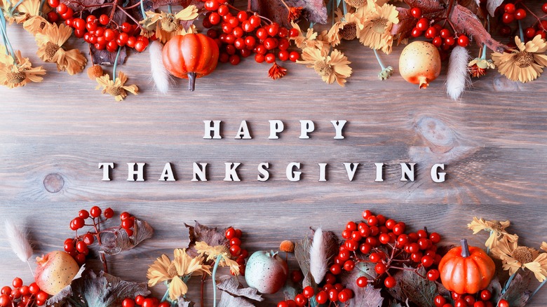 Happy Thanksgiving message surrounded by autumnal produce and flowers on wooden table