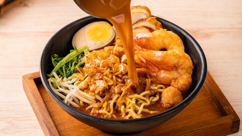 Broth pouring over prawn noodles