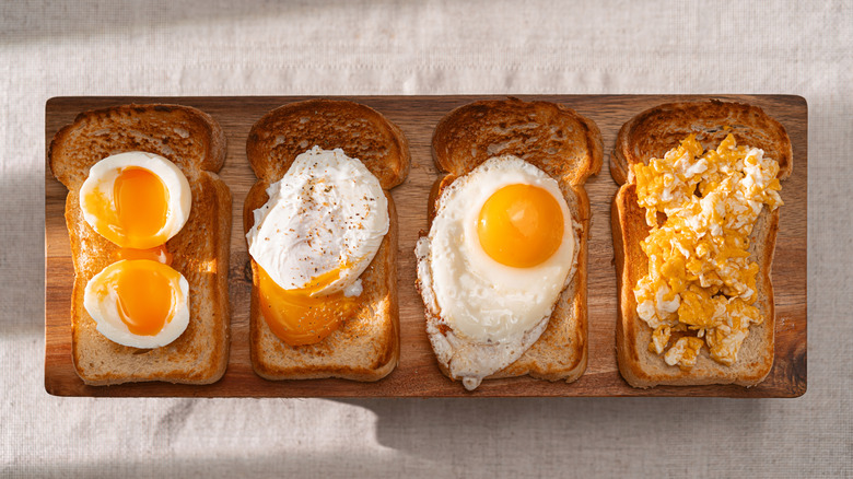 four pieces of toast on a board with different styles of cooked eggs