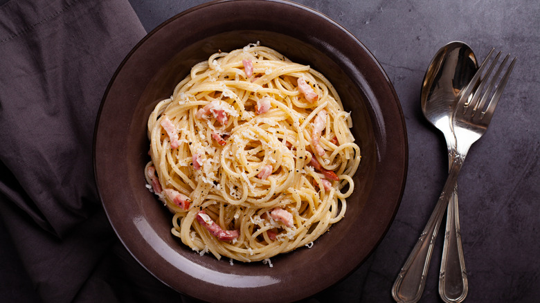 a bowl of spaghetti carbonara pasta next to utensils