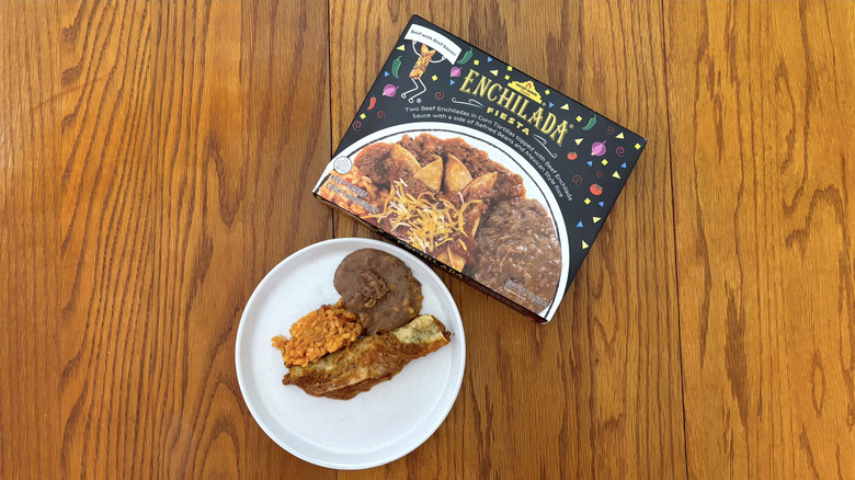 Night Hawk beef enchilada with beef sauce and spanish rice and refried beans on white plate on wooden table