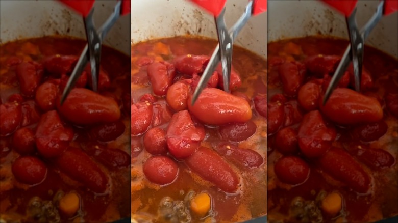 Cutting canned tomatoes with scissors in a pot