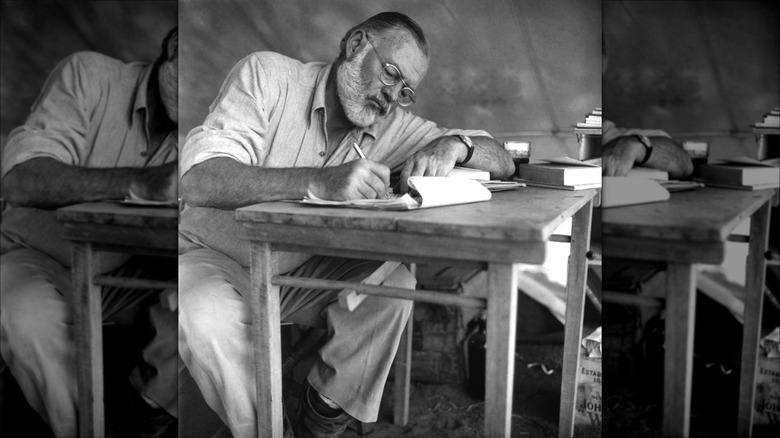 Black and white photo of Ernest Hemingway writing at desk