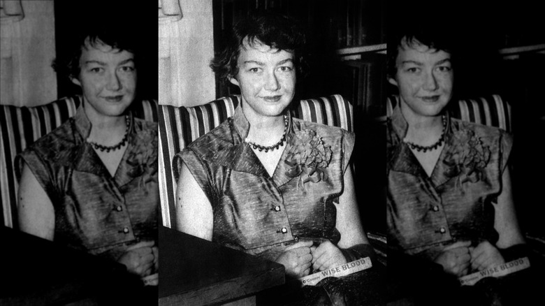 Photo of Flannery O'Connor sitting in armchair holding book Wise Blood