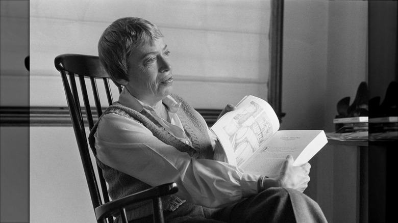 Black and white portrait of Ursula Le Guin sitting in chair holding open book