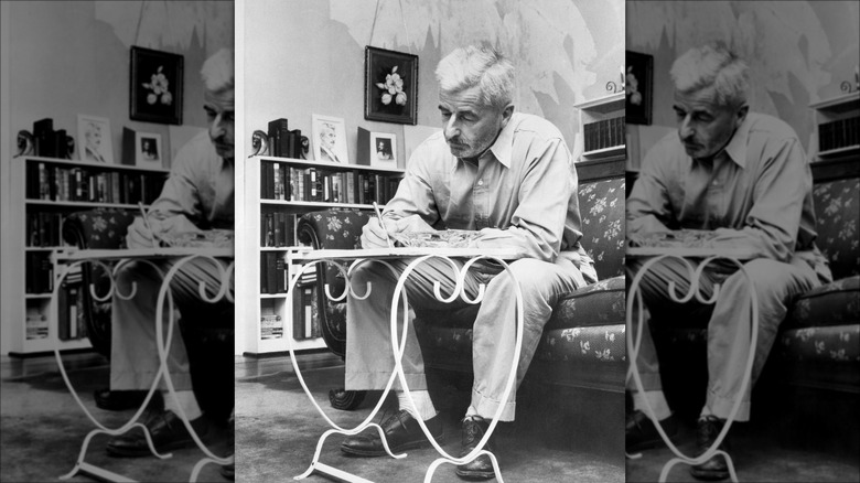 Black and white portrait of William Faulkner sitting in chair hunched over writing desk