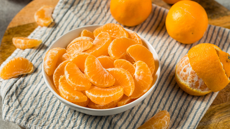 Bowl of mandarin orange segments surrounded by whole oranges