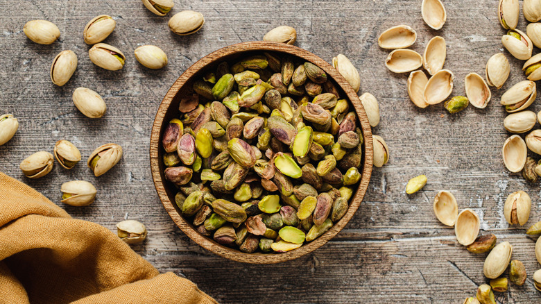 wooden bowl of shelled pistachios surrounded by whole pistachios