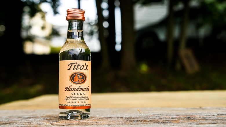 Tito's vodka bottle sitting ona  wooden surface outside