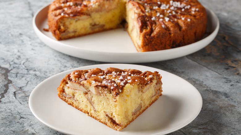 Slice of eplekake on a plate with a cake in the background