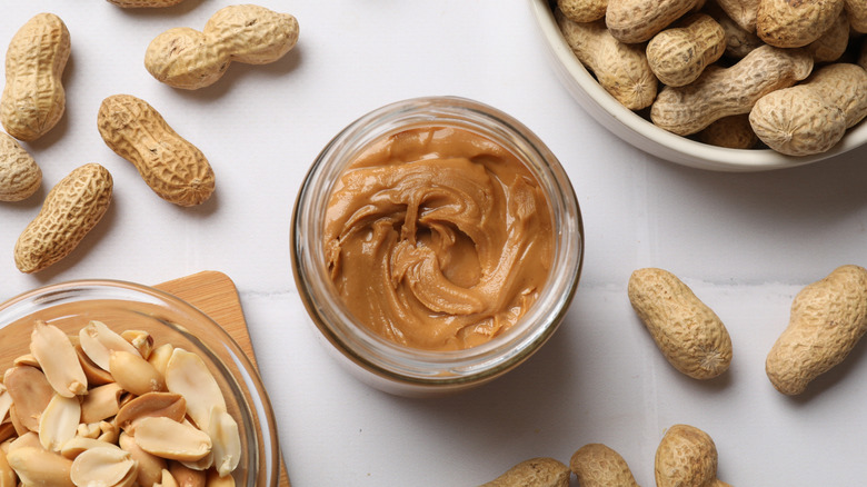 Peanut butter in jar with peanuts on the side