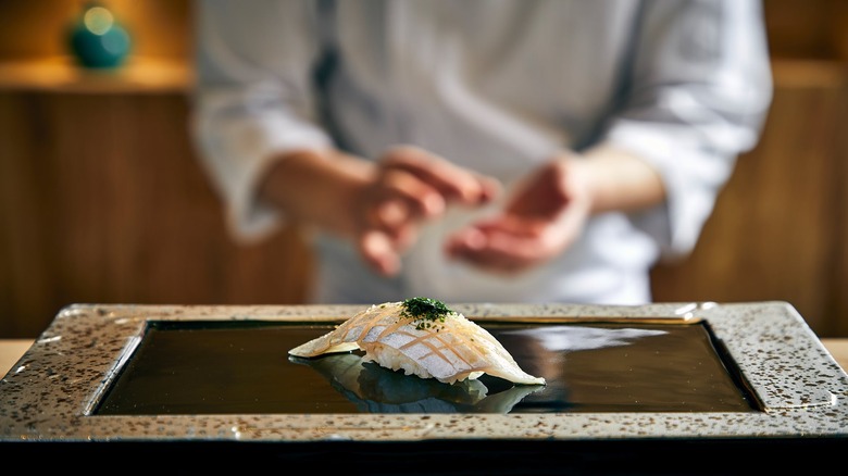 Edomae-style sushi roll with a blurred chef in the background at Omakase Yume