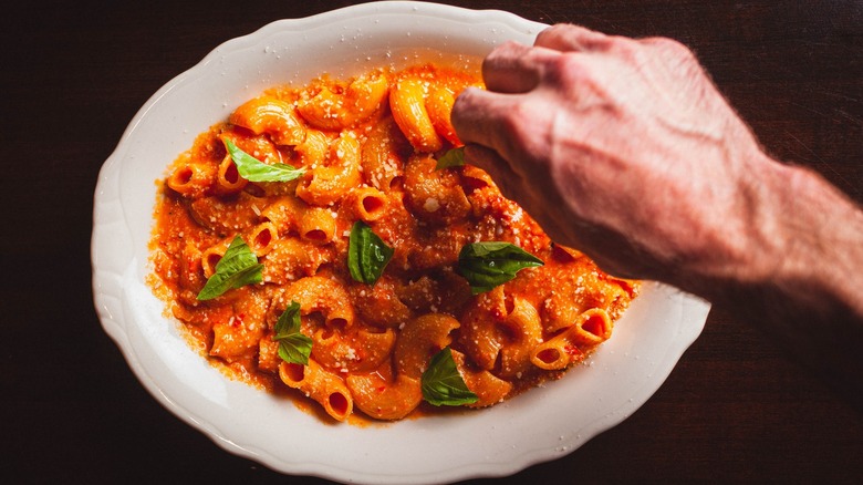 Hand putting basil leaf on elbow pasta with red sauce at Trivoli Tavern