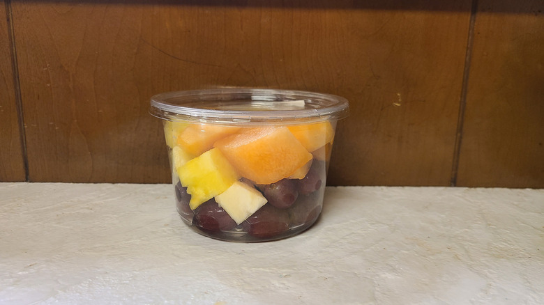 Plastic cup of grapes, pineapple, and cantaloupe in front of wooden background