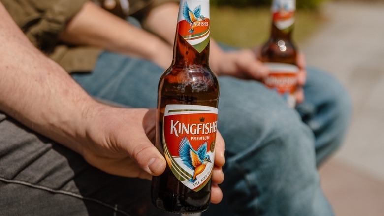 A bottle of Kingfisher beer being held by two men as they sit down