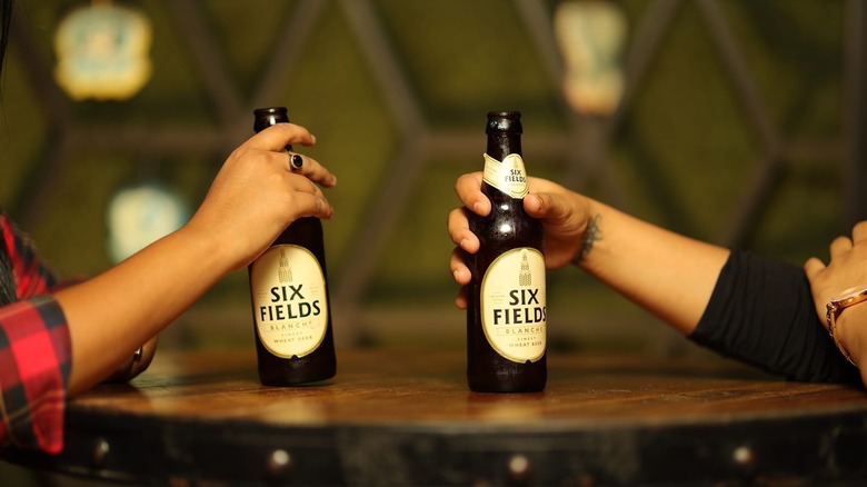 Two people holding bottles of Six Fields Blanche at a table