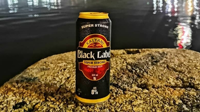 A can of Kalyani Black Label resting on a rock in front of a body of water