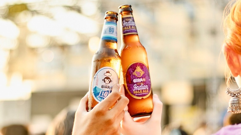 Two people holding up two different bottles of Bira 91