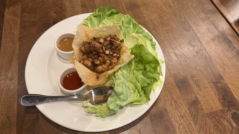 A fried tortilla shell has chicken, lettuce, and two dipping sauces on a wood table.