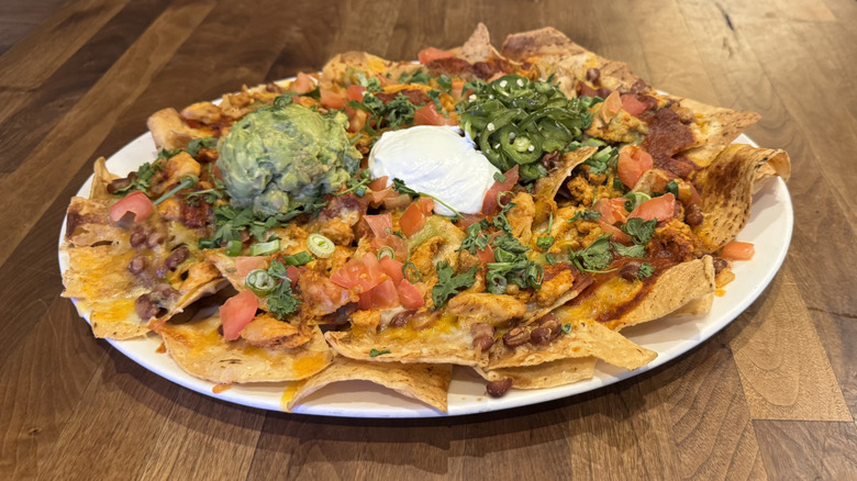 A white plate is filled with chicken nachos with guacamole and sour cream.