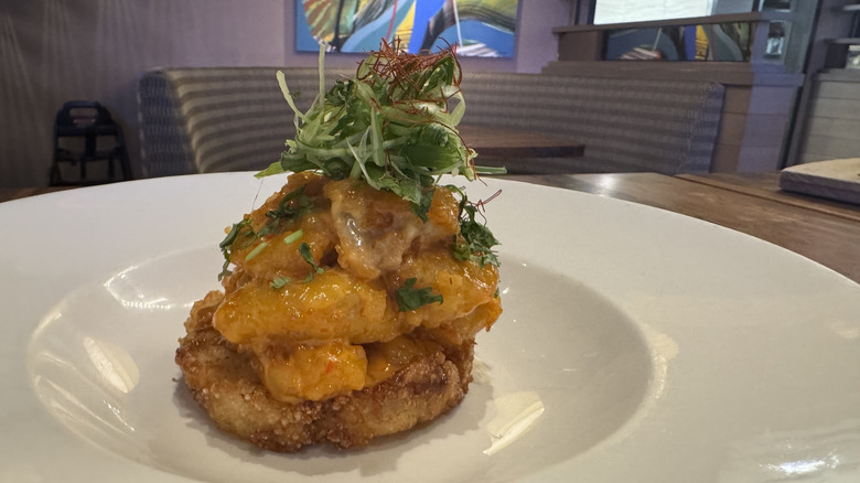 A white plate has a crispy rice cake and fried shrimp with cucumber garnish on top.