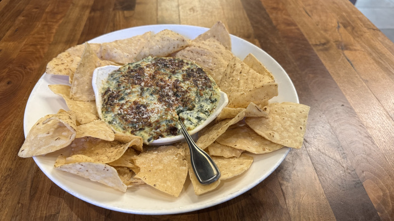 A white plate is filled with tortilla chips and spinach dip.