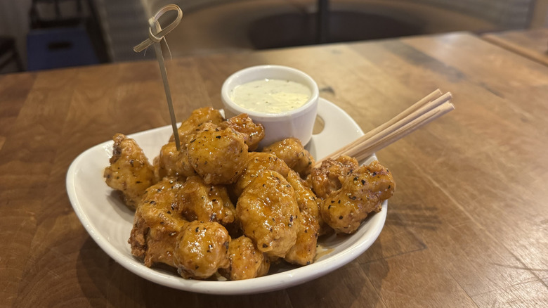 Vegetarian Buffalo wings sit on small white plate on a table with vegan ranch sauce.