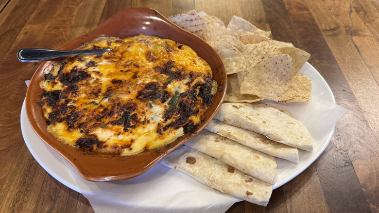 Melted cheese dip with soft tortillas is on a white plate on a wood table.