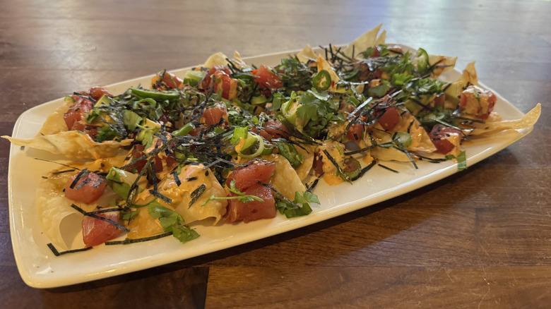 A white rectangular plate has crispy wontons and raw tuna with green onions and seaweed.