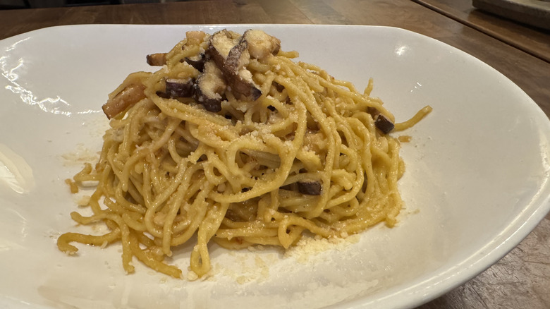 A white plate full of noodles and cheese is topped with shitake mushrooms.