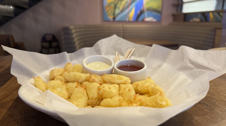 Fried cheese curds with dipping sauces are on a white plate lined with paper.