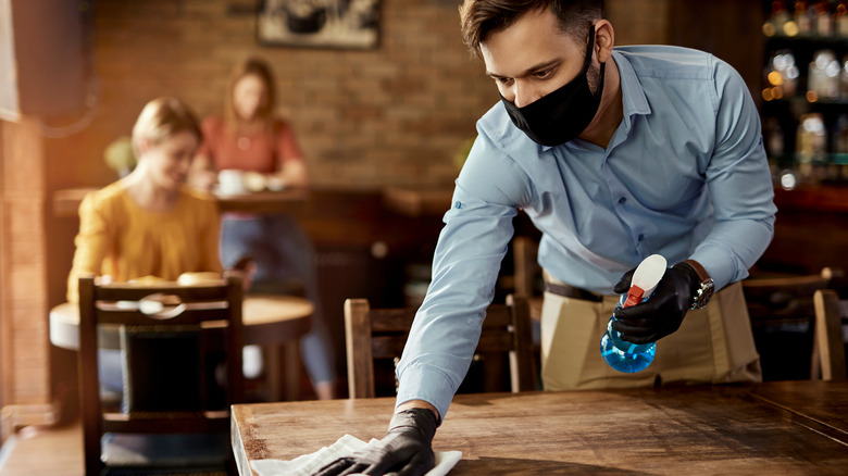 Person cleaning tables wearing mask