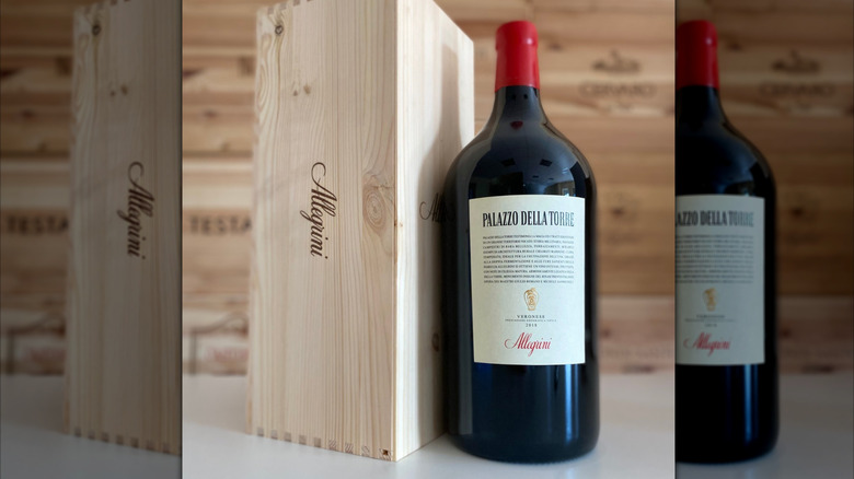 large Italian red wine bottle standing next to a wooden box on a white counter and wood boxes in the back