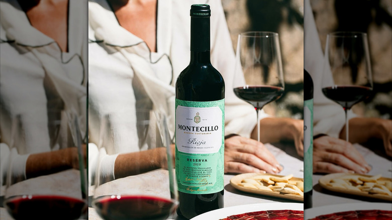 bottle of Rioja red wine with snacks and two glasses and a person in the background holding the glass