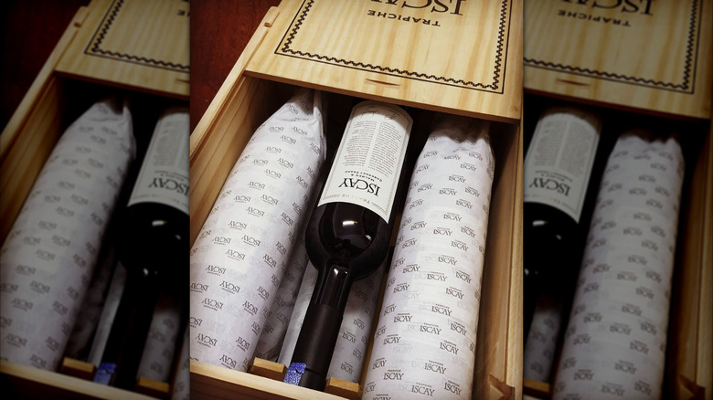 wooden crate packed with red wine bottles wrapped in paper and one unwrapped bottle in the center