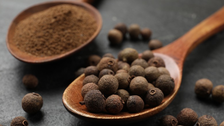 A scoop of ground allspice next to a scoop of whole allspice