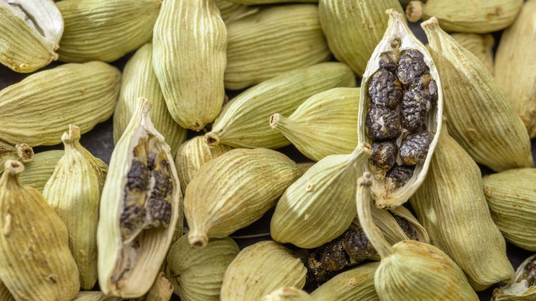 Two opened cardamom pods in a pile of pods