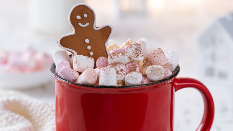 Gingerbread man in mug of hot chocolate with marshmallows and sprinkle of cinnamon.