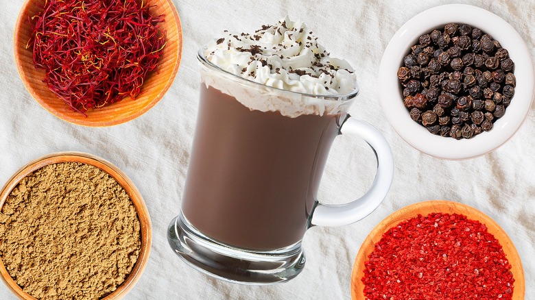 Glass mug of hot chocolate with whipped cream, surrounded by spices